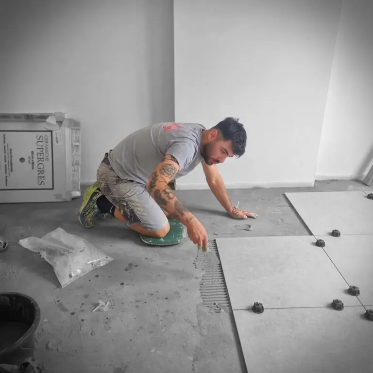 Lorenzo Muratore à genoux sur un chantier de rénovation, en train de poser du carrelage