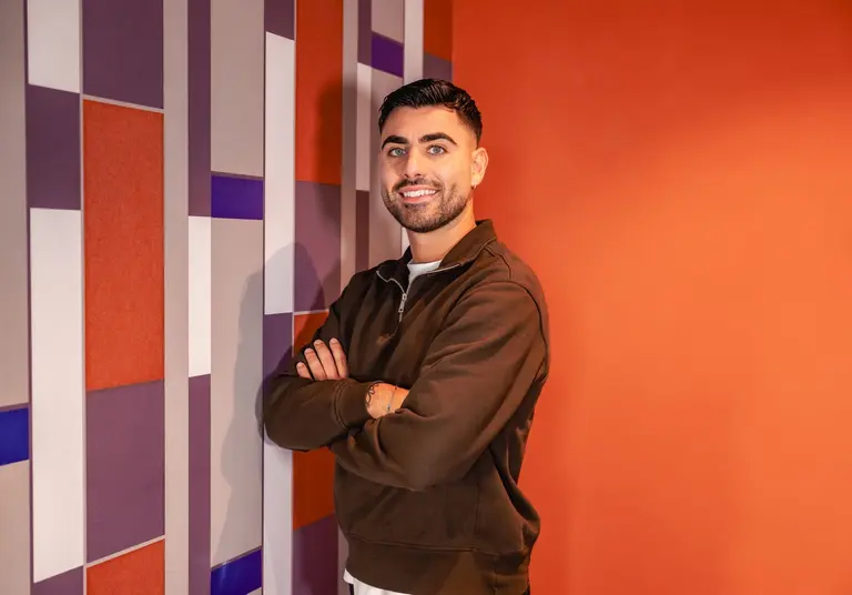 Lorenzo Muratore, coach en investissement immobilier en Belgique, souriant bras croisés devant un mur orange